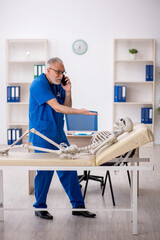 Wall Mural - Old male doctor examining skeleton in the clinic