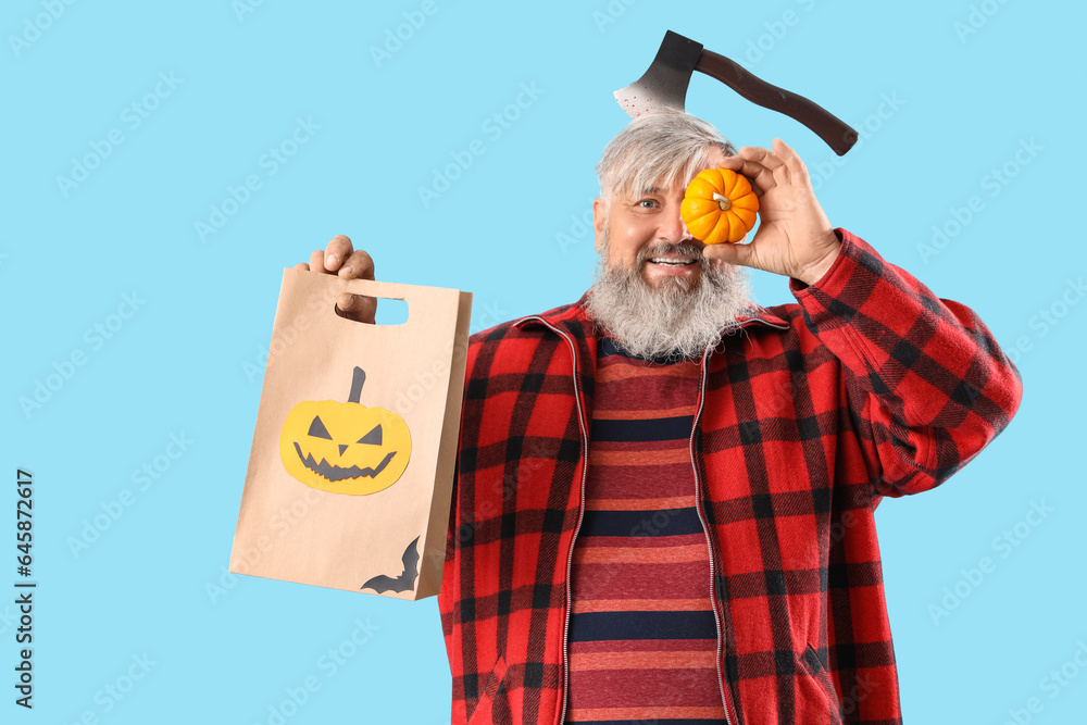 Mature man dressed for Halloween with pumpkin and gift bag on blue background