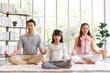 © aekkorn - Young; asian family with daughter sit on floor practice yoga together; happy parents with girl child rest on floor meditate relieve negative emotions on weekend at home.