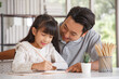 © aekkorn - Children education and home school concept : Young asisn father pleased to see little daughters' study success. Excited smiling small child girl enjoying learning and writing with pleasant dad at home