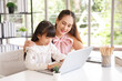© aekkorn - Children education and home school concept : Young asian mother pleased to see little daughters' study online. Excited smiling child girl enjoying online learning  with pleasant mom at home.