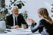 © gstockstudio - Happy mature man in formalwear interviewing job candidate while sitting at the office desk together
