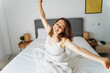 © olezzo - Young happy beautiful woman stretching while sitting on bed in the morning