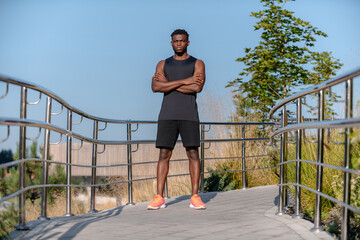 Canvas Print - Handsome African man in sportswear keeping arms crossed and looking at camera while standing outdoors