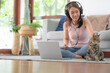 © interstid - Happy Asian woman working at home using laptop computer while palying with cat