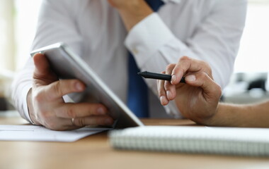  Focus on male hand holding stylos. Colleague with modern tablet explaining conditions of contract. Businessmen discussing new start-up. Business meeting concept. Blurred background