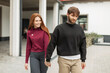 © alones - Beautiful fashionable couple in fashion clothes hold hands and walk on the street. Pretty cute red-haired girl and a handsome hipster man in a hoodie outdoors
