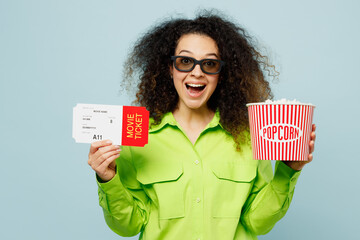 Wall Mural - Young excited happy surprised shocked cool latin woman in 3d glasses wear green shirt casual clothes watch movie film hold in hand ticket bucket of popcorn in cinema isolated on plain blue background.