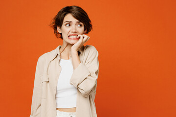 Wall Mural - Young sad mistaken displeased caucasian woman she wears beige shirt casual clothes look aside on area biting nails fingers isolated on plain orange red background studio portrait. Lifestyle concept.