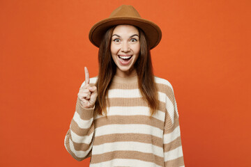 Sticker - Young proactive woman she wears striped sweater hat casual clothes holding index finger up with great new idea isolated on plain orange red color wall background studio portrait. Lifestyle concept.