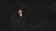 © TimmyTimTim - An unknown man in hood jacket using cellphone in dark background. Hacker, scammer or criminal using smartphone to lure victim, cyber criminal concept.