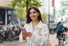 Mixed-race LGBT Proud And Confident Turkish Young Woman Holding A Phone In The Street Smiling Wearing White Casual Clothes