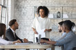 © fizkes - Confident african American businesswoman stand lead team company meeting with colleagues in office, biracial female leader boss talk brainstorm with coworkers at briefing, cooperation concept