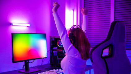 Wall Mural - Winning Victory. Asian gamer playing online video game excited on desktop computer PC colorful neon LED lights, woman in gaming headphones use computer she happy successful, E-Sport concept, back view