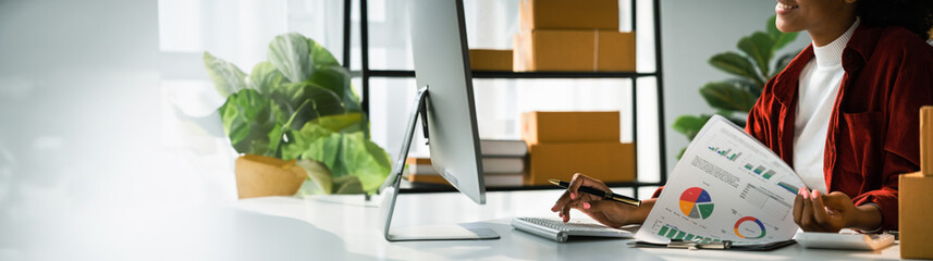 African american woman reading business document and working on computer for delivery online order