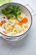 Creamy soup with italian tortellini and chicken fillet, vertical shot on a white granite background, middle closeup