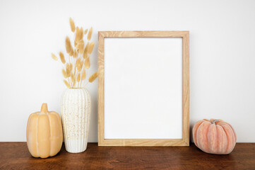 Wall Mural - Mock up portrait wooden frame with fall grasses and pumpkin decor on a wood shelf against a white wall. Autumn concept. Copy space.
