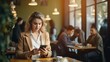 © Suleyman - Young freelancer woman in business attire utilizing smartphone and laptop while seated at table in cafe with people in background blur