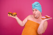 Early morning. Funny fat man gets ready to eat a burger after a shower. Pink background.