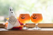 Pumpkin Beer In Jack-o-lantern Glasses Sitting Alone Side A Ghost With A Tag, "Boo" Text. Outdoor Seating Area Of A Restaurant Bar.