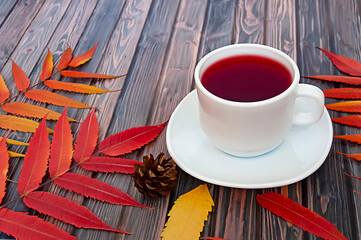 White cup of natural tea with rose hips on a wooden background with autumn leaves. Autumn lifestyle