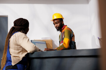 Wall Mural - Postal service employees checking parcels invoice list on computer while chatting at checkout. African american man and woman storehouse coworkers supervising inventory management