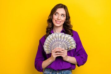 Poster - Portrait of cute satisfied girl with wavy hairstyle wear violet blouse hold money look at offer empty space isolated on yellow background