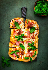 Wall Mural - Hot Roman pizza with ham, pancetta, mozzarella cheese, sun dried tomatoes, sauce and green basil, rustic green table background, top view