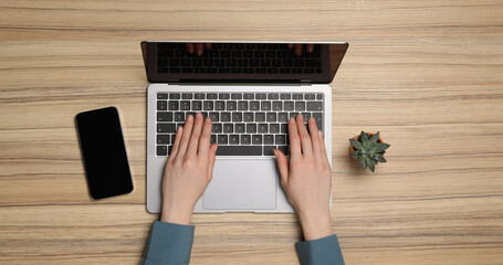 Wall Mural - Woman using laptop at wooden table, top view