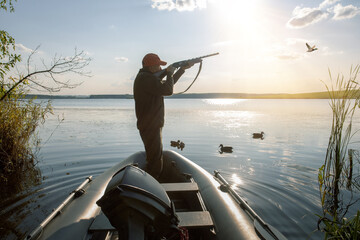 Wall Mural - Waterfowl hunter in boat. hunter shooting to the flying duck at sunrise.