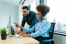 Friendly Smiling Woman Call Center Operator With Headset Using Computer, Customer Service, Call Center Worker Accompanied By Her Team At Office.