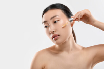 Canvas Print - Beautiful young woman applying cosmetic serum onto her face on white background, space for text