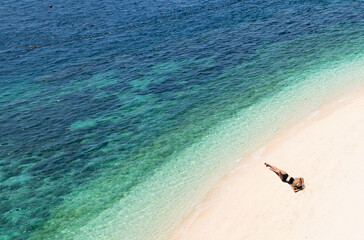 Wall Mural - Aerial view of beautiful young woman in black swimsuit lying on sandy beach near blue sea with waves at sunset Summer vacation at Andaman Island