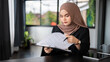 © bongkarn - A professional adult Asian Muslim businesswoman is examining business documents at her desk.