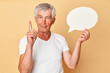 Your words can fill this empty speech bubble. Inspired gray haired senior man pensioner wearing white T-shirt isolated over beige background raised finger up having idea warming