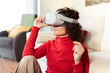 © Westend61 - Smiling woman wearing virtual reality headset sitting at home