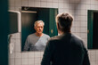 © Westend61 - Senior man looking in mirror in bathroom