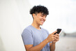 © mimagephotos - smiling young man using cellphone by white wall