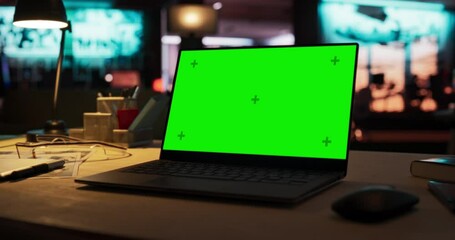 Leinwandbilder - Zoom in of Mock-up Green Screen on a Laptop Standing on the top of a Wooden Table. In the Background Stylish Modern Office Studio in the Evening with Neon Lights. Desk of Creative Designer