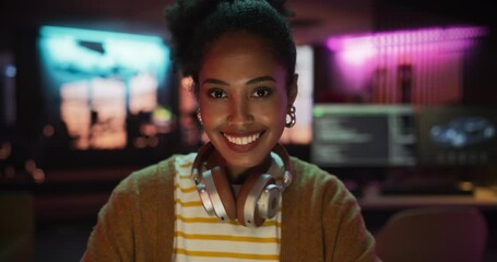 Poster - Close Up Portrait of a Young Black Woman with Headphones, Looking at Camera, and Smiling in a Creative Office. Beautiful Diverse Female Working for her Dream Agency, Feeling Empowered