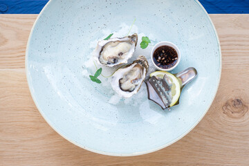 Two fresh oysters on plate with lemon and mignonette sauce in a restaurant