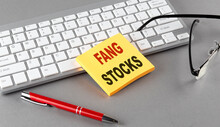 FANG STOCKS text on a sticky with keyboard, pen glasses on grey background