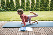 Little girl 5-6 years old stretching in Tiger Pose, or Vyaghrasana on the roll mat practicing yoga outdoors