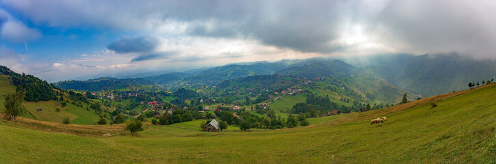 Wall Mural - Rural idyllic landscape of the small villages in the Rucar-Bran mountain area, Brasov, Romania, scattered on the wooded hills, with the Bucegi mountains in the background, in wonderful springtime day