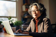 © InputUX - An Asian senior woman sits confidently at her desk, her face illuminated by the laptop screen. A smile crosses her face, showcasing her ease and happiness while navigating technology.
