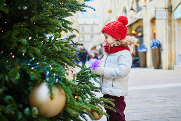 Wall Mural - Adorable preschooler girl near Christmas trees decorated with golden baubles in Paris, France