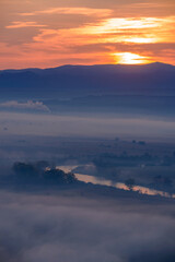 Wall Mural - Aerial view of the sunrise over the valley in beautiful early morning mist in the highlands. Low clouds and fog cover the sleeping meadow. Hills valley mists landscape. Serene moment in rural area