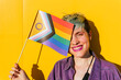 © VISTA by Westend61 - Cheerful lesbian woman covering eye with rainbow flag in front of yellow wall