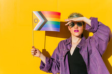 Lesbian Woman Shielding Eyes And Holding Rainbow Flag In Front Of Yellow Wall
