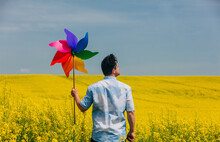Man Holding Colorful Pinwheel Toy In Rapeseed Field